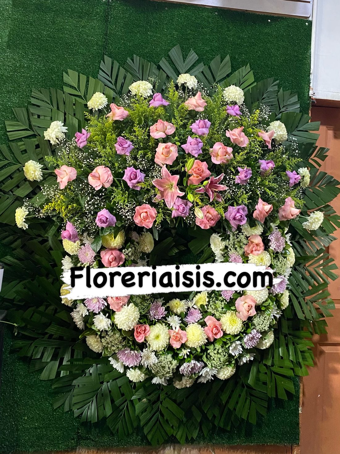 Corona fúnebre de flores rosas, lilas y blancas sobre fondo de pasto