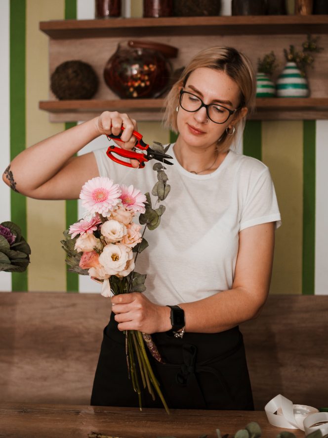 Florista cortando tallos de un ramo de gerberas rosas en el taller