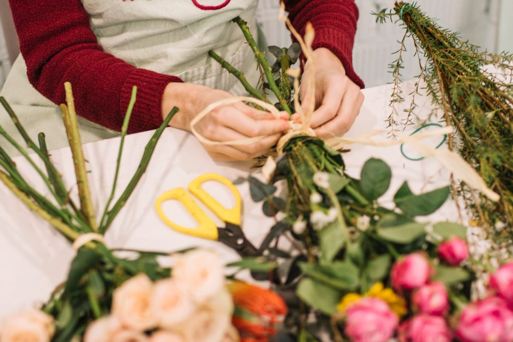 Manos de florista atando un ramo con rafia sobre la mesa de trabajo
